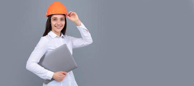 Hapy woman in protective hard hat helmet with laptop computer isolated on grey background Architect