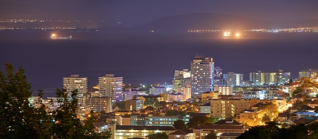 Harbour buildings and city at night with lights urban development and streets Dark travel and outdoor residential architecture of downtown with ocean or sea water in the evening with a skyline