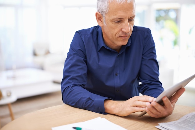 Hard aan het werk, zelfs thuis Shot van een volwassen man die thuis een digitale tablet gebruikt