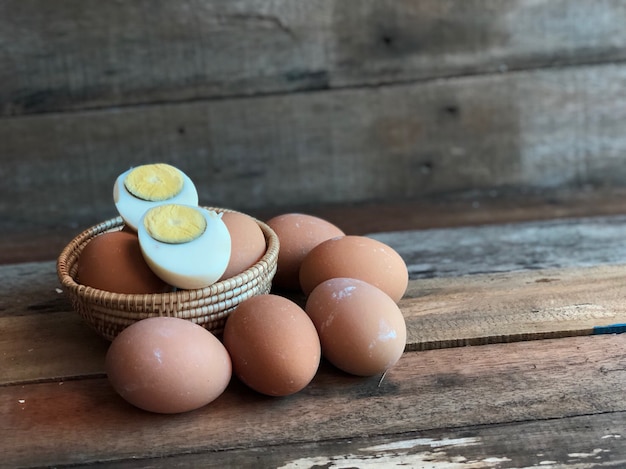 Hard-boiled egg and knife on wooden board, pile of eggs in wicker basket on old wood 