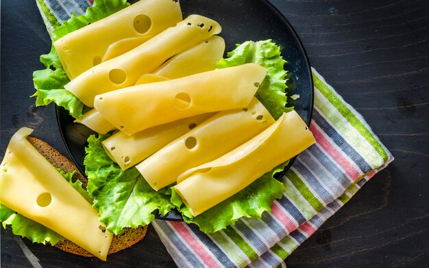 Твердый сыр с большими дырочками, нарезанный на тарелке с листьями салата