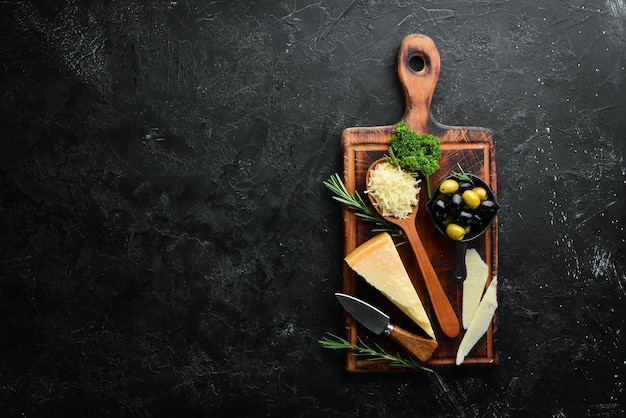 Hard cheese with olives and cheese knife on black stone background Parmesan Top view Free space for your text