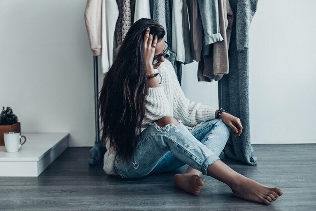 Hard choice.  Thoughtful young woman in casual wear sitting on the floor at home 