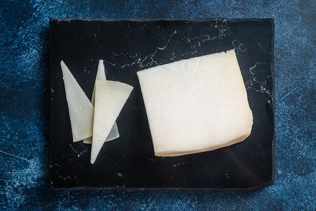 Hard goat cheese on marble board Blue background Top view