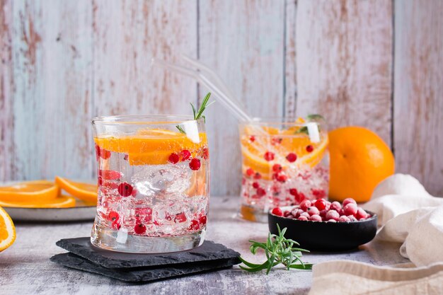 Hard seltzer alcoholic cocktail with orange berries and rosemary in glasses on the table