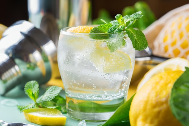 Hard seltzer cocktail with lemon, mint and ice on a table. Summer refreshing beverage, drink with trendy zero waste accessories, bamboo straw and mesh bag.