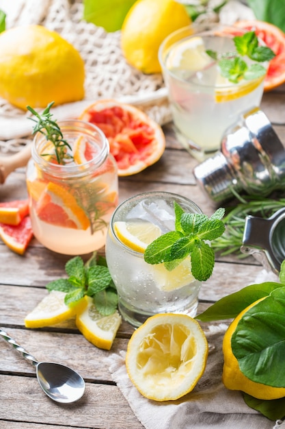 레몬, 자몽, 민트, 로즈마리 및 얼음을 테이블에 얹은 하드 셀처 칵테일. 여름의 상쾌한 음료, 트렌디 한 제로 폐기물 액세서리, 대나무 빨대 및 메쉬 백.