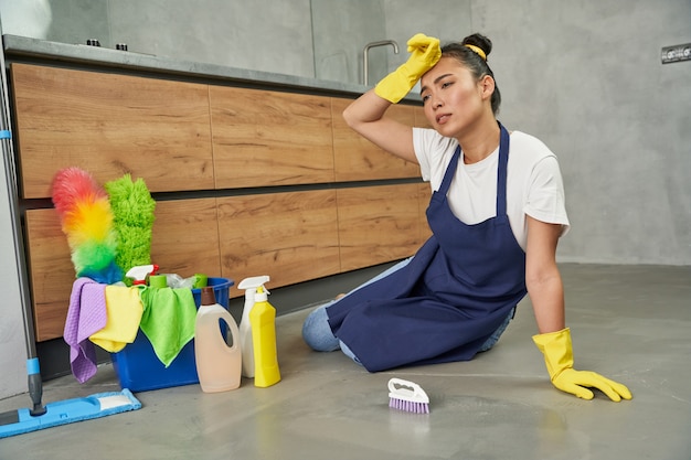 Hard werken full-length shot van vermoeide, uitgeputte jonge vrouw die uitrust tijdens het schoonmaken