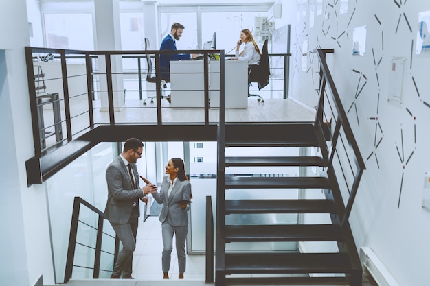 Hard working employees working at firm. Two of them sitting at table and working while other two climbing the stairs and talking.