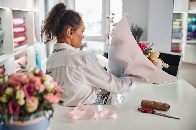 花のスタジオで完成した花の構成を運ぶ勤勉な女性