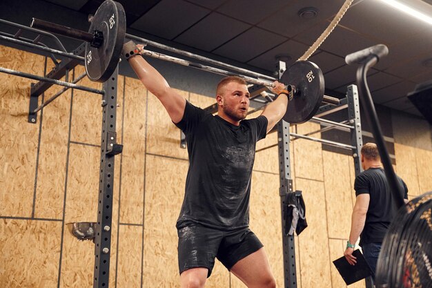 Foto harde gezichtsuitdrukking proberen sterke man tilt barbell op in de sportschool