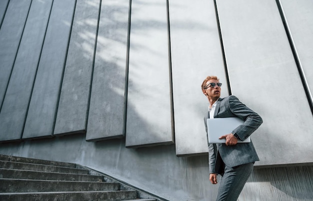 Hardlopen en naar het werk gaan Jonge zakenman in grijze formele kleding is buiten in de stad