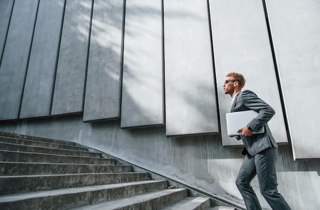 Hardlopen en naar het werk gaan Jonge zakenman in grijze formele kleding is buiten in de stad