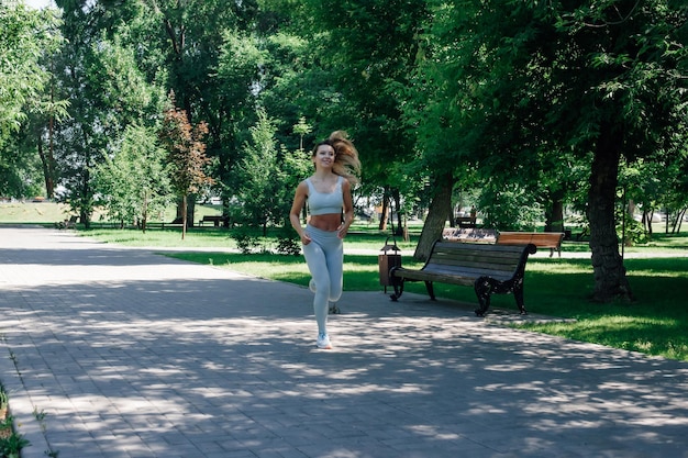 Hardlopen snel lachende jonge sportieve vrouw opwarmen rekken in grijze sportkleding in park in zonnige zon...