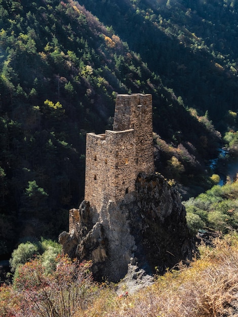 Hardtoreach ancient battle towers on the rocks Sunny afternoon in the Caucasus mountains Medieval tower on green mountain forest background Ingushetia region