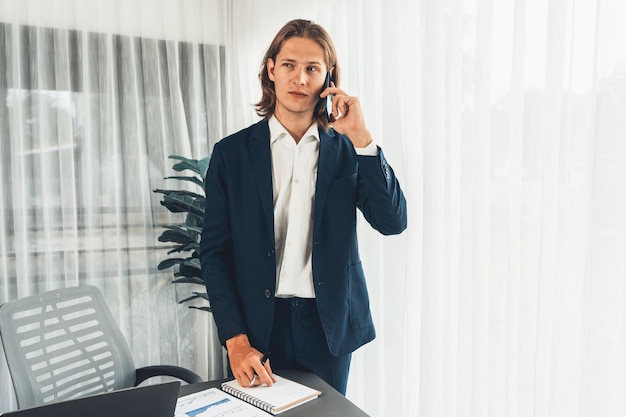 Hardwerkende zakenman staat in een modern kantoor en praat aan de telefoon.