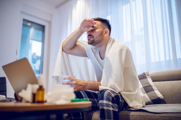 Hardworking employee in pajamas and covered with blanket having fever.