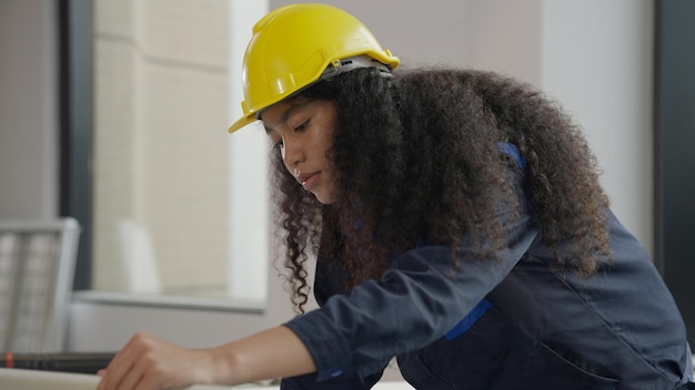 Hardworking female architect with yellow helmet drawing on blueprint