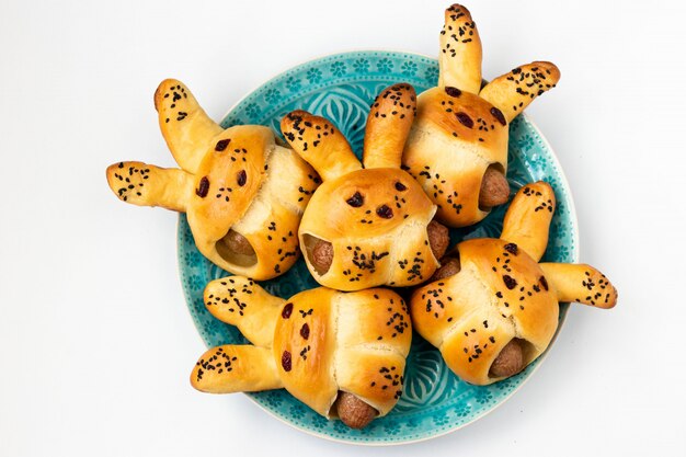 Hare-shaped buns with sausages for children located on a blue plate on a white background, a culinary idea for children