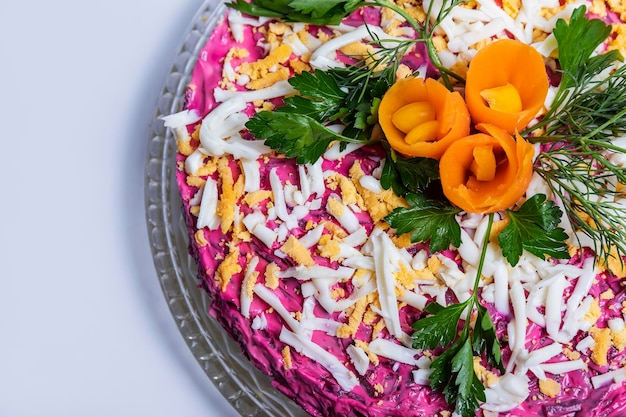 Haringsalade onder een bontjas op een glazen schaal op een witte tafel.