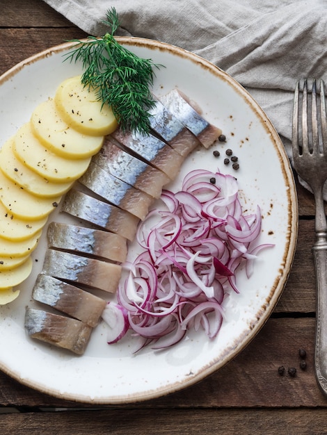 Haringvis met aardappelschijfjes en rode ui op tafel met vork en keukenhanddoek.