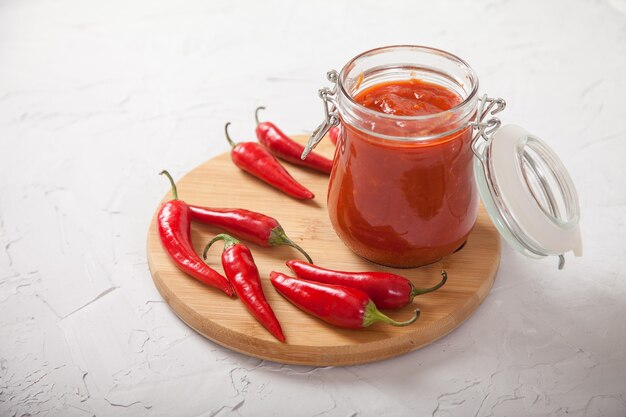 Harissa in een glazen pot op een houten standaard en hete chilipepers.