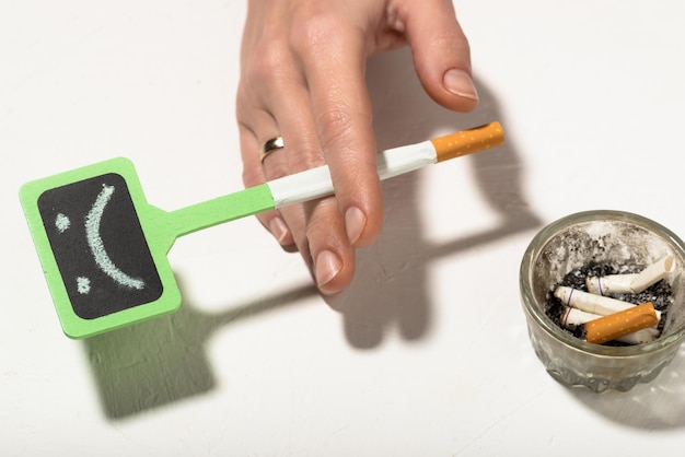 흡연 개념의 해로움 불행한 스마일리와 여성의 손에 든 담배 흡연은 흡연으로 인한 건강에 해롭고 나쁜 습관 우울증입니다