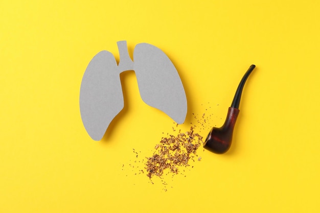 黄色の背景に喫煙パイプとタバコを吸う肺の害