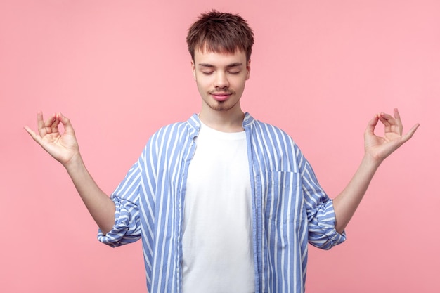 Harmonie in het leven. Portret van een rustige bruinharige man met een kleine baard en snor in een casual gestreept shirt met opgeheven hand, meditatiegebaar met vingers. studio-opname geïsoleerd op roze achtergrond