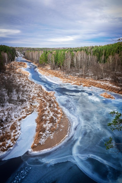 Harsh winter nature landscape with wintry river covered with ice going through snowy pine forest