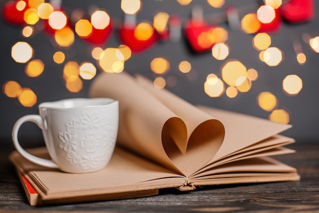 Hart gemaakt van boekbladen met een kopje in lichten, liefde en valentijn concept op een houten tafel