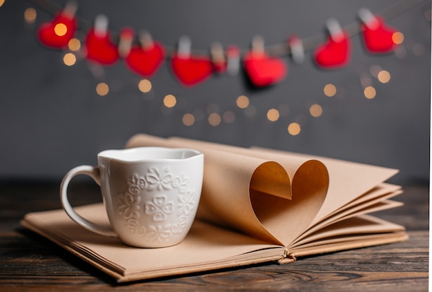 Hart gemaakt van boekbladen met een kopje in lichten, liefde en valentijn concept op een houten tafel