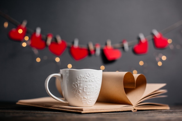 Hart gemaakt van boekbladen met een kopje in lichten, liefde en valentijn concept op een houten tafel