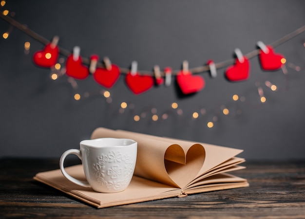 Hart gemaakt van boekbladen met een kopje in lichten, liefde en valentijn concept op een houten tafel