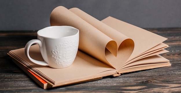 Hart gemaakt van boekbladen met een kopje, liefde en valentijn concept op een houten tafel