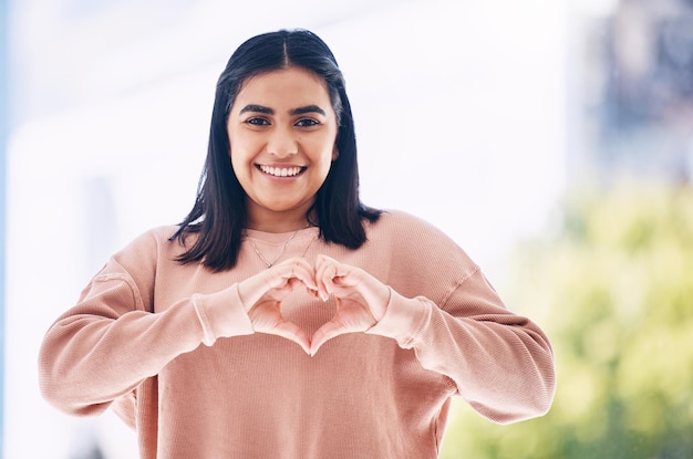 Hart handen portret en gelukkige vrouw voor zelfzorg cardiologie wellness en gen z ondersteuning voor de gezondheid van vrouwen Gezicht van een jonge Indiase persoon met liefde emoji teken of gebaar voor zoals stemmen en glimlachen