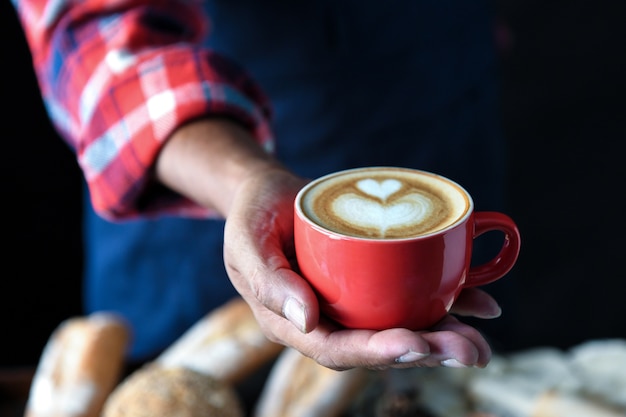 Hart koffie latte in rode kop verzonden vanuit de hand.