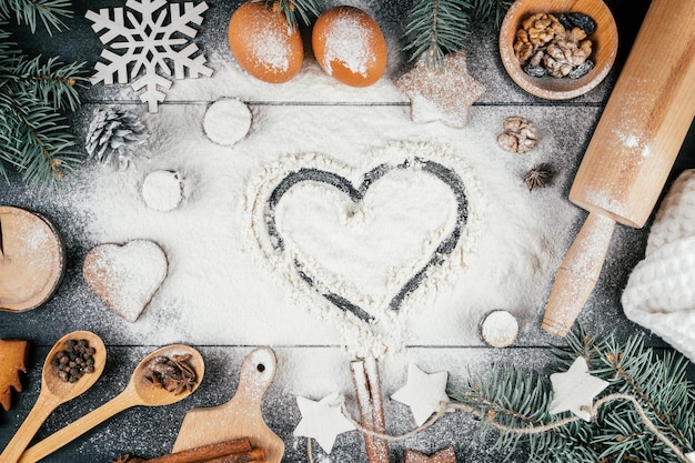 Hart op bloem op zwarte tafel met takken van kerstboom, bakaccessoires en ingrediënten. ruimte kopiëren. bovenaanzicht.