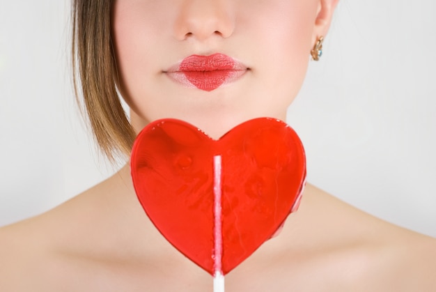 Hart op lippen van mooie vrouwenclose-up met hartlolly