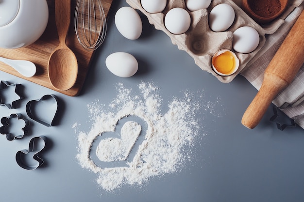 Hart van meel en kookgerei. Concept van Valentijnsdag. Zelfgemaakte koekjes maken voor Valentijnsdag, plat, bovenaanzicht. Ingrediënten voor het bakken op een grijze achtergrond.