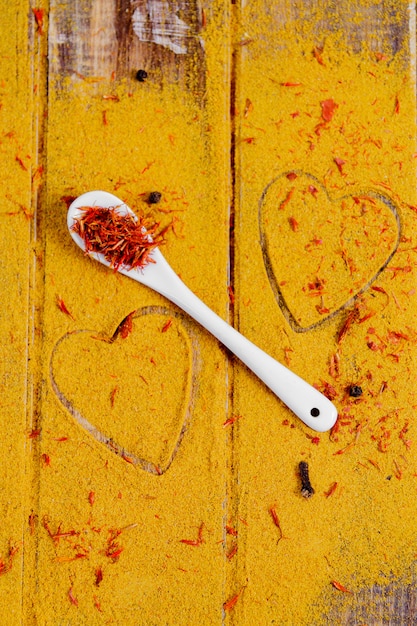 Foto hart van specerijen en kruiden. witte lepel met saffraan op kerrie