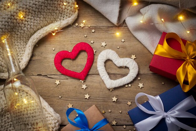 harten, gebreide sjaal, geschenkdozen, lichtgevende slinger op een houten achtergrond.