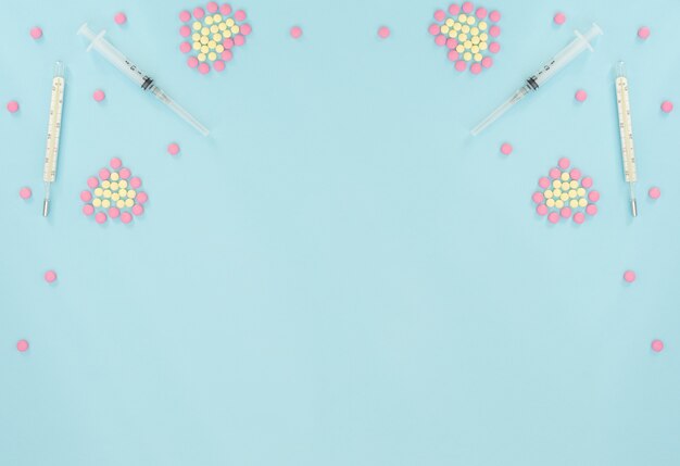 Harten gemaakt van roze en gele pillen, thermometer, spuit op lichtblauwe achtergrond