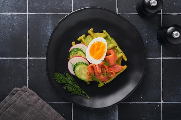 Hartige wafels Ontbijt groene wafels wilde knoflook of spinazie met ei tomaat zalm op houten plaat voor ontbijt op oude zwarte tegel tafel achtergrond Licht diner lunch of ontbijt Bovenaanzicht