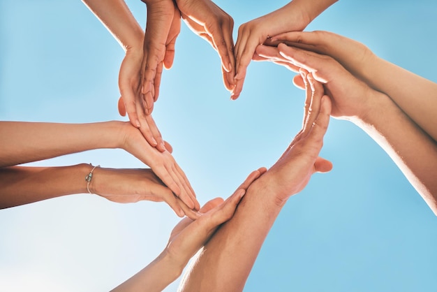 Hartliefde en groepshanden voor ondersteuning, zorg en gemeenschap met buiten zomerzon, blauwe lucht en mock-up Groep mensen met zorgteken voor solidariteit, gezondheid en welzijn achtergrondmodel