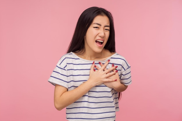 Hartproblemen Portret van brunette meisje in gestreepte tshirt geklemd borst en schreeuwen van plotselinge acute pijn hartaanval infarct binnen studio opname geïsoleerd op roze achtergrond