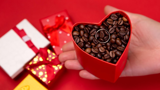 Hartvorm cadeau met gebrande koffiebonen en trouwring op rode achtergrond
