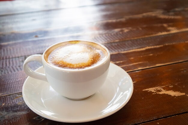 Hartvorm latte art in witte koffiekopje op houten tafel in café-restaurant