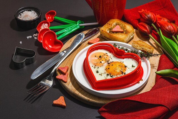 Hartvormig gebakken ei geserveerd met geroosterd brood en kruiden op een bord Romantisch kunstvoedselidee voor Valentijnsontbijt Harde lichte donkere schaduw zwarte steen betonnen achtergrond kopie ruimte