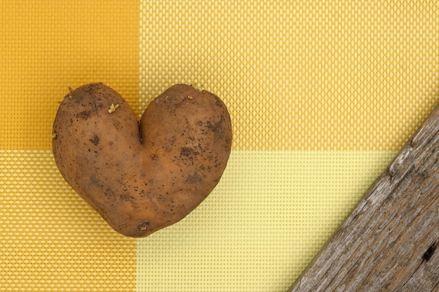 Foto hartvormige aardappel op gele tafel naast verweerd hout als lintbanner